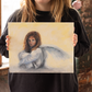 A model holding an 11x14" original oil painting of an angry angel. 