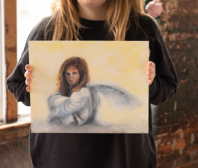 A model holding an 11x14" original oil painting of an angry angel. 